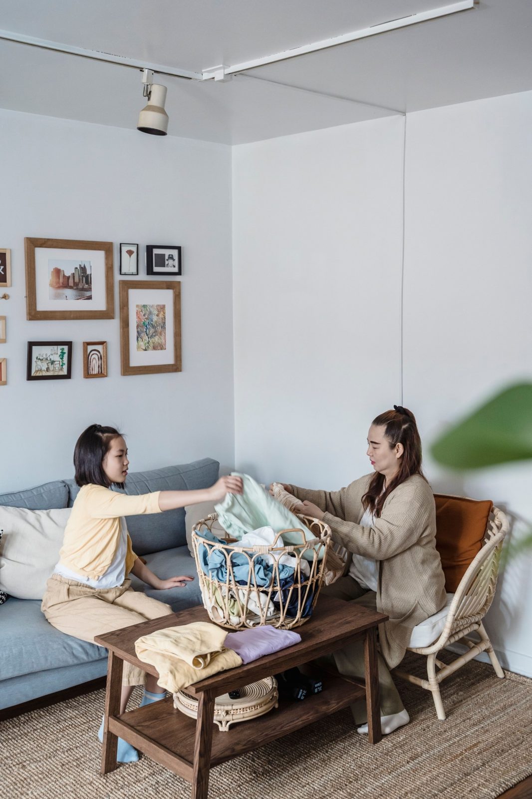Two people fold washing together on a couch, a basket of clean clothes between them.